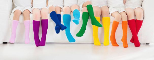 Kinder tragen bunte Regenbogensocken. Kinderschuhkollektion. Eine Vielzahl von gestrickten kniehohen Socken und Strumpfhosen. Kinderkleidung und Kinderbekleidung. Kindermode. Beine und Füße von kleinen Jungen und Mädchen. - Foto, Bild