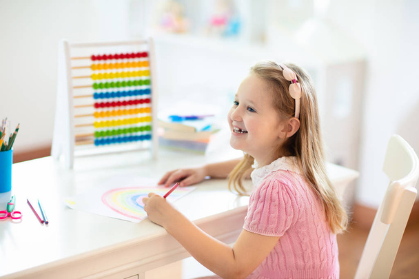 Child drawing rainbow. Kid painting at home. Little girl doing homework after school. Kids desk with abacus in white sunny bedroom. Children study, learn to read and write. Bedroom for young student. - Fotografie, Obrázek