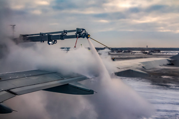 ein Prozess des Sprühens von vereisungsschutzweißer Flüssigkeit der hintere Teil des Flügels eines Flugzeugs auf dem Flughafen bei Sonnenaufgang im Winter ist am blauen Himmel mit rosa Wolken Hintergrund. - Foto, Bild