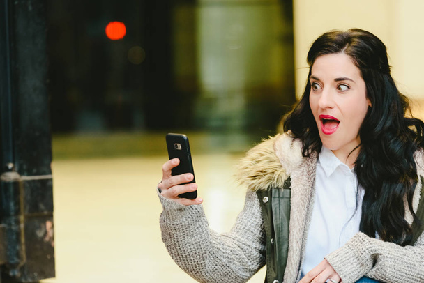 Woman surprised to receive good news by his mobile phone, expression and surprise gestures. - Photo, Image