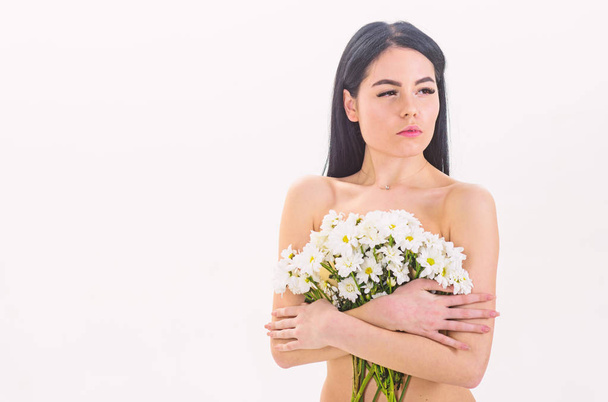 Woman with smooth healthy skin looks attractive. Natural cosmetics concept. Lady covers breasts with flowers, isolated on white. Girl on calm face naked holds chamomile flowers in front of breasts - Photo, Image