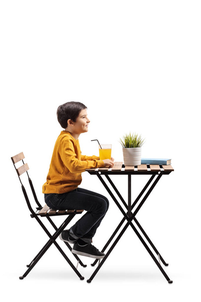Full length profile shot of a little boy sitting at a table with an orange juice isolated on white background - Fotoğraf, Görsel