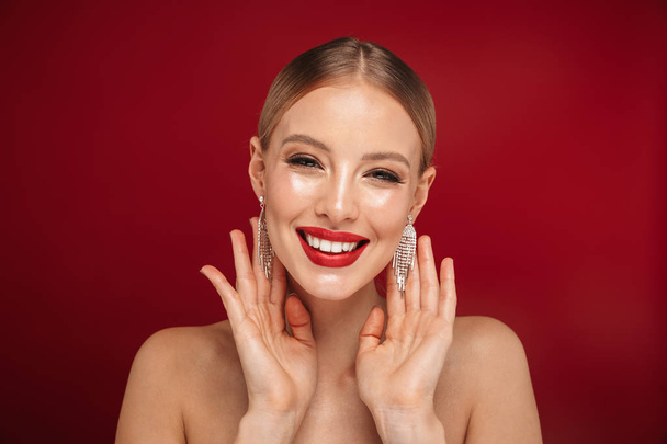 Beauty portrait of a pretty young topless woman standing isolated over red background, wearing accessories, posing - Φωτογραφία, εικόνα