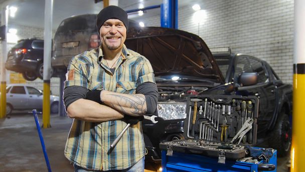 Autoservice. Brutale mechanic man permanent door de auto en glimlachen - Foto, afbeelding