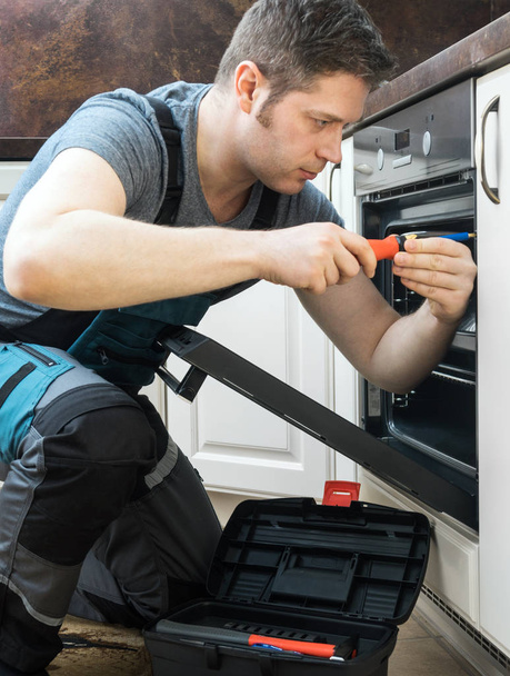 Handwerker in Overalls repariert Haushaltsbackofen in der Küche. - Foto, Bild