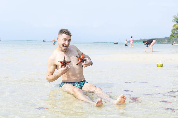 Travel boy is sitting on the sea with red starfishes makes funny photos in Phu Quoc island in crystal clear water - Photo, image