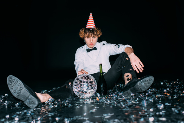 homme aux cheveux bouclés assis dans la casquette de fête avec boule disco isolé sur noir
 - Photo, image