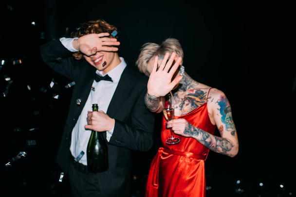 couple covering face while holding alcohol drinks on party isolated on black - Photo, Image