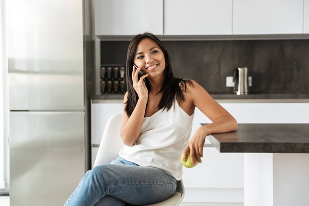 Photo of adorable asian woman resting in apartment and talking on mobile phone while sitting on chair - Photo, image