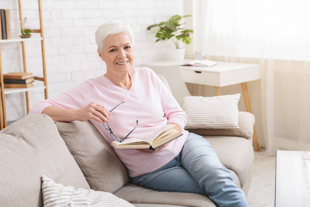Idősebb nő, pihent a kanapén, és könyvet olvas - Fotó, kép