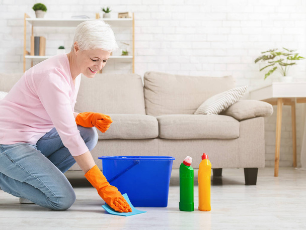 Χαμογελώντας ώριμη νοικοκυρά καθαρισμού δαπέδου στο σπίτι - Φωτογραφία, εικόνα