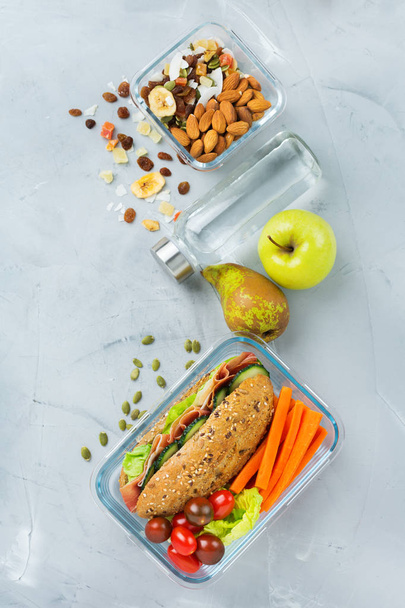 Food and drink, still life, diet and nutrition, healthy eating, take away concept. Lunch box with sandwich, fruits, vegetables, nut mix and bottle of water. Top view flat lay background - Zdjęcie, obraz