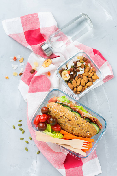 Essen und Trinken, Stillleben, Ernährung und Ernährung, gesunde Ernährung, Konzept zum Mitnehmen. Lunchbox mit Sandwich, Obst, Gemüse, Nussmischung und einer Flasche Wasser. Ansicht von oben flacher Hintergrund - Foto, Bild