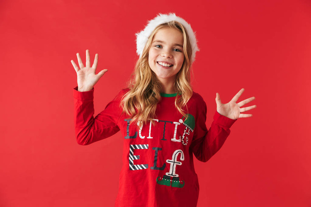 Cheerful little girl wearing Christmas costume standing isolated over red background, celebrating - Foto, immagini