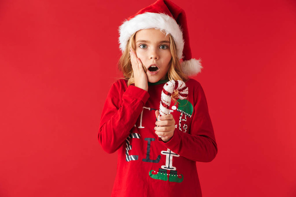 Shocked little girl wearing Christmas costume standing isolated over red background - 写真・画像