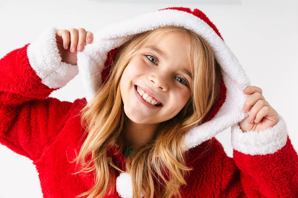Cute cheerful little girl wearing Christmas costume isolated over red background - Фото, изображение
