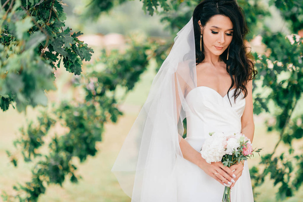beautiful bride in white dress posing with bouquet of flowers in hands - Fotó, kép