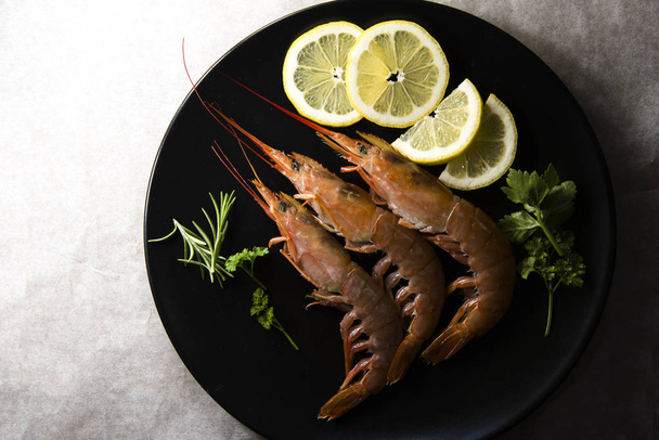 prawns and slices of lemon on a black plate - Photo, Image