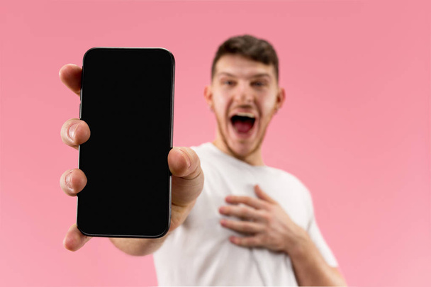 Young handsome man showing smartphone screen isolated on pink background in shock with a surprise face - Zdjęcie, obraz