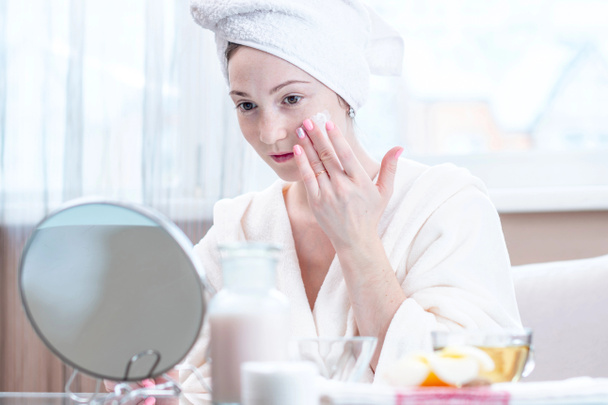 Piękny szczęśliwy młoda kobieta z ręcznikiem na głowie stosowania kremu naturalnych kosmetyków na twarzy nawilżenie skóry. Pojęcie higieny i pielęgnacji skóry w domu - Zdjęcie, obraz
