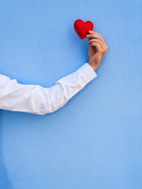 Grußkarte für einen fröhlichen Valentinstag mit Kopierplatz für Text. rotes Herz in der Hand eines Mannes auf blauem Hintergrund - Foto, Bild