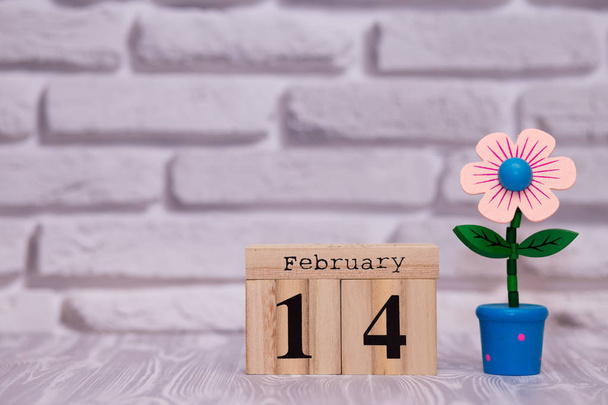 14 Φεβρουαρίου. Ημέρα 14 του μήνα στο ξύλινο ημερολόγιο με λουλούδι παιχνίδι σε φόντο λευκό τούβλο. Happy Ημέρα του Αγίου Βαλεντίνου. - Φωτογραφία, εικόνα