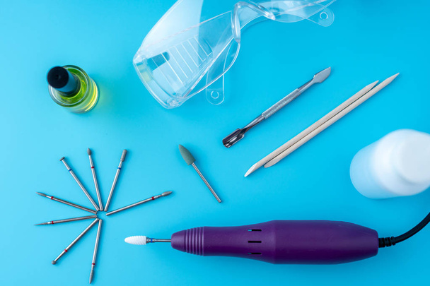 A set of cosmetic tools for professional hardware manicure on a blue background. Milling cutter, glasses, cuticle cleanser, top view - Valokuva, kuva