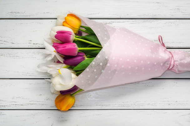 Bouquet of multicolored tulips in paper wrapper on white wooden table. - Фото, изображение