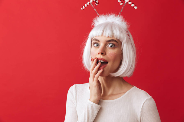 Image of an excited young shocked woman dressed in carnival christmas costume posing isolated over red wall background. - Фото, изображение