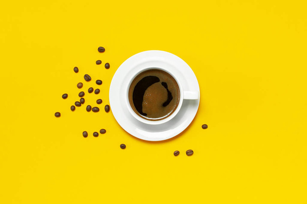 Rovnou položit šálek černé kávy a kávových zrn na žlutém pozadí pohled shora kopie prostoru. Koncept minimalistických potravin, ráno snídaně, čas práce, teplé nápoje, káva pozadí. - Fotografie, Obrázek