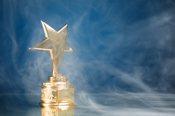 Gouden sterren trofee in rook, blauwe achtergrond - Foto, afbeelding
