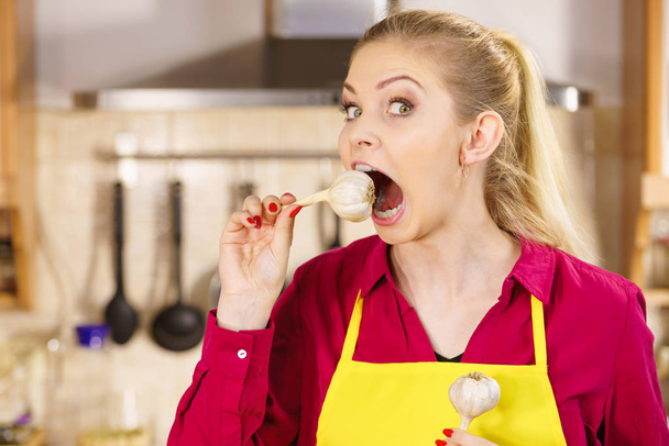Grappige jonge vrouw probeert te eten rauwe knoflook neemt een grote hap met wijd open mond. - Foto, afbeelding