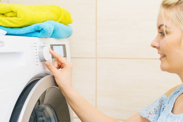 Young blonde woman setting washing clothes laundry machine knob, choosing program. Household duties concept. - Фото, зображення