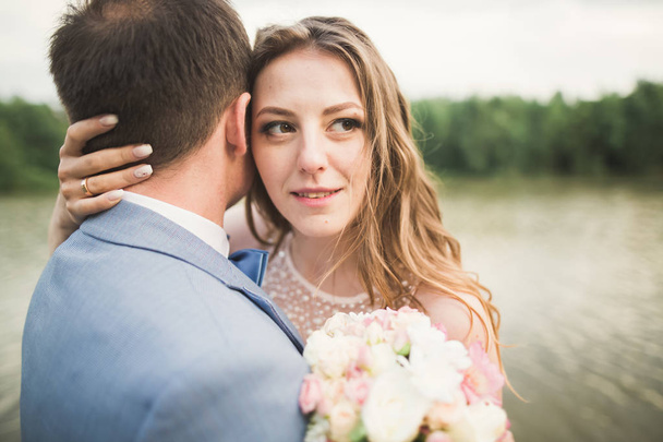 Bride and groom holding beautiful wedding bouquet. Lake, forest - Foto, Imagen