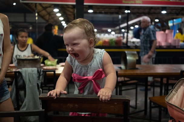 Μωρό χαμογελά και κοιτώντας ψηλά σε φωτογραφική μηχανή. κοριτσάκι γελάει σε ένα καφέ το βράδυ διαβολική γελάς - Φωτογραφία, εικόνα