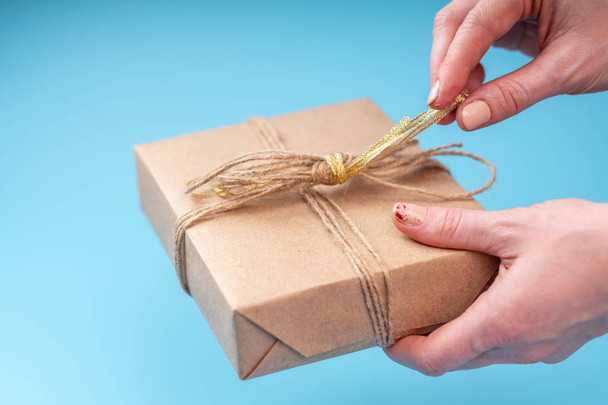 Руки держат подарочную коробку упакованную в бумагу Крафта на синем фоне. Открытка на день Святого Валентина и женский день
 - Фото, изображение