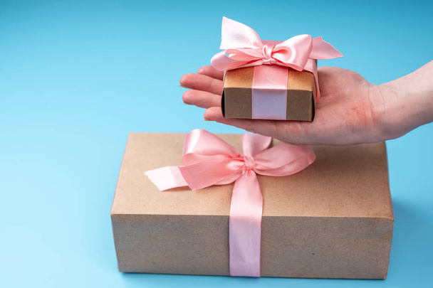 Жіноча руки проведення подарунковій коробці Запаковані в Крафт-папір з рожевою стрічкою на блакитному тлі. Концепція святкова листівка для закоханих і дню жіночого дня - Фото, зображення