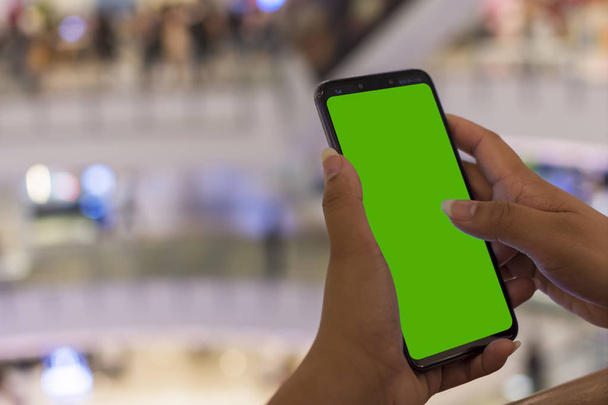 woman holding modern smartphone with green screen for replacement with blur background department store - Photo, Image