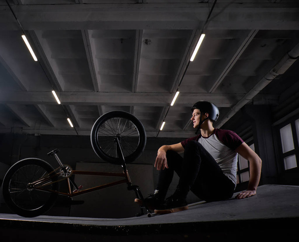 Bmx всадник расслабляется после практики трюки с велосипедом в скейтпарке в помещении
 - Фото, изображение