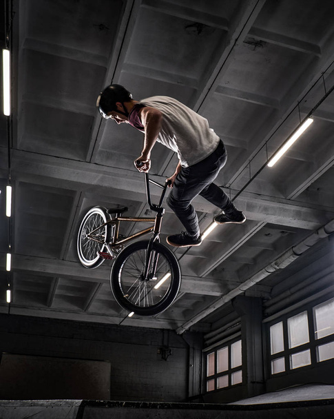 Young BMX making crazy tricks on his bicycle in skatepark indoors. - Fotó, kép