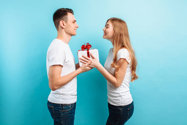 Loving couple man and woman, stand with gift box, happy couple on a light blue background. Valentine's Day - Фото, изображение