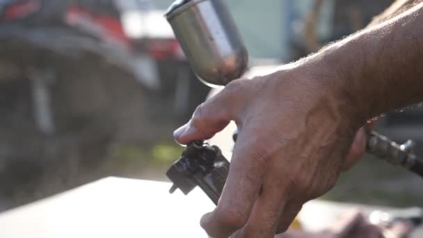 Ręce mechanika myje szczegółów samochodu przez rozpylanie wody. Człowiek używa sprayem do jego pracy. Osoba zajmująca się naprawami pracy na zewnątrz. Niewyraźne tło. Dołu widok zwolnionym tempie z bliska - Materiał filmowy, wideo