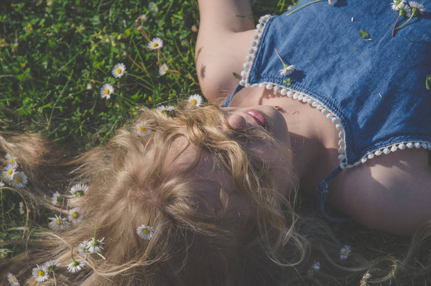 мила дівчина з довгим світлим волоссям, що лежить серед ромашок у зеленій траві на лузі
 - Фото, зображення