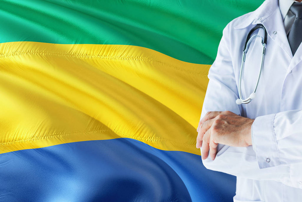Gabonese Doctor standing with stethoscope on Gabon flag background. National healthcare system concept, medical theme. - Foto, Bild