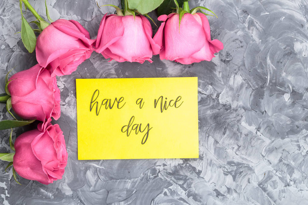 Concetto romantico. rose rosse e lettering che desiderano avere una bella giornata su uno sfondo grigio cemento
. - Foto, immagini
