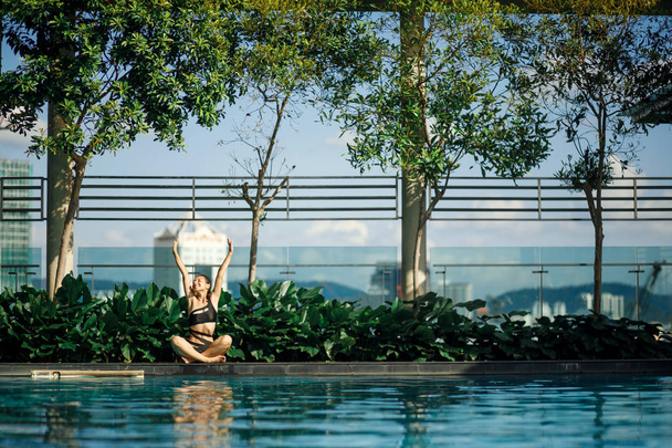 Sexy magro caucasiano morena esticar-se entre arbustos verdes e árvores na borda da piscina no telhado com paisagem urbana
. - Foto, Imagem