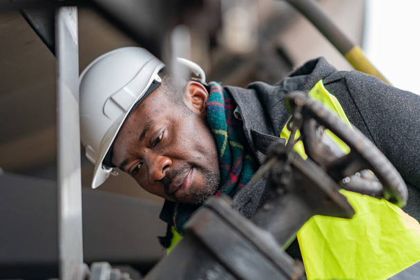 Mécanicien afro-américain portant un équipement de sécurité (casque et veste) vérifier et inspecter train d'engrenages - Photo, image