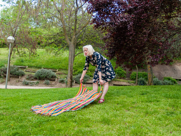 Женщина кладет полотенце на траву на зеленом газоне
  - Фото, изображение