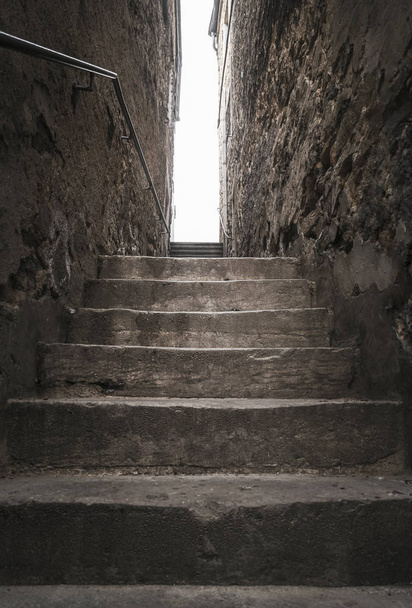 Gealterte Steintreppen, zwischen zwei alten Gebäuden, hinauf, dem Licht entgegen, in der Stadt Luxemburg. Starkes Licht am Ende der schattigen Treppe. - Foto, Bild