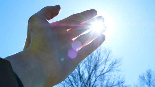 Hand van man vingers speelt met de zonnen stralen tegen de blauwe hemel - Foto, afbeelding